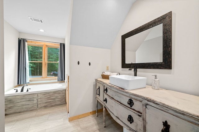 bathroom with vanity, lofted ceiling, and tiled bath