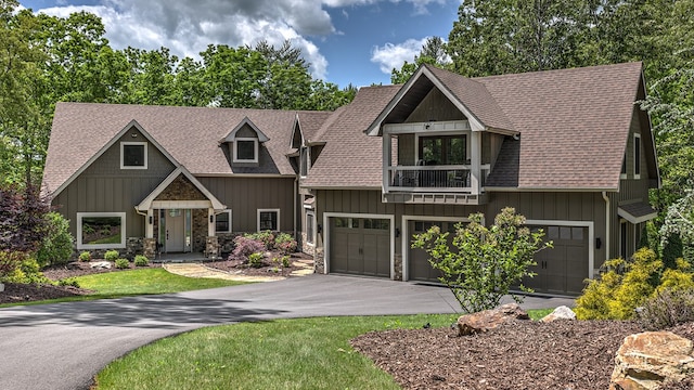 craftsman-style home featuring stone siding, driveway, a garage, and a balcony