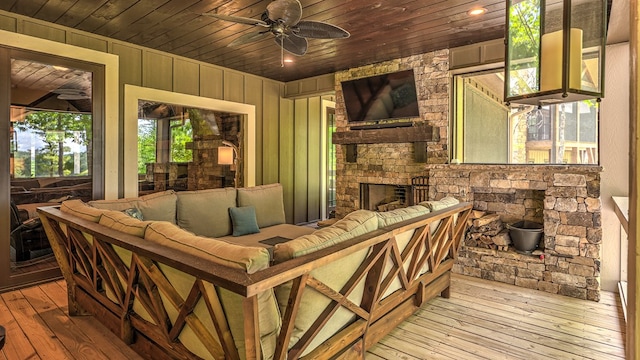 exterior space with wooden walls, wood-type flooring, a ceiling fan, wood ceiling, and a stone fireplace