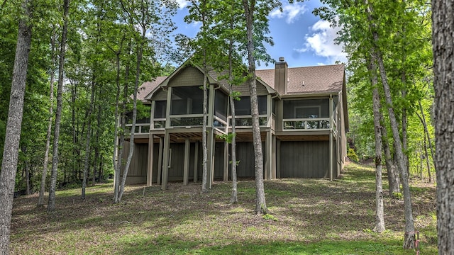 rear view of property featuring a chimney, a sunroom, and a shingled roof