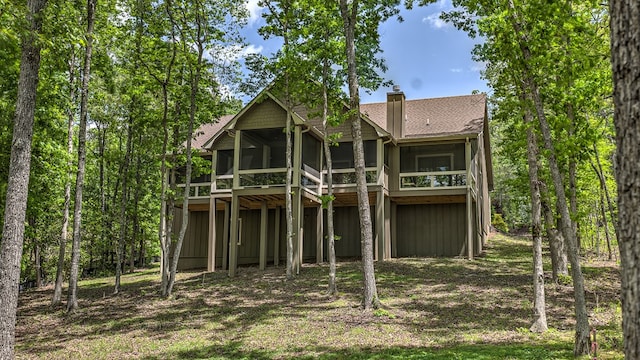 back of house featuring a sunroom, a shingled roof, and a chimney