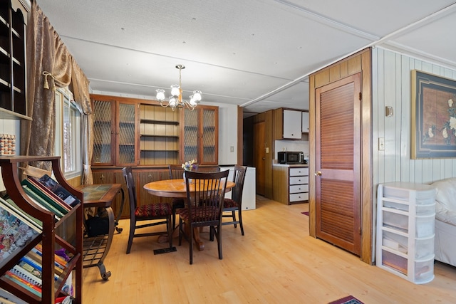 dining space featuring wooden walls, a chandelier, and light hardwood / wood-style flooring