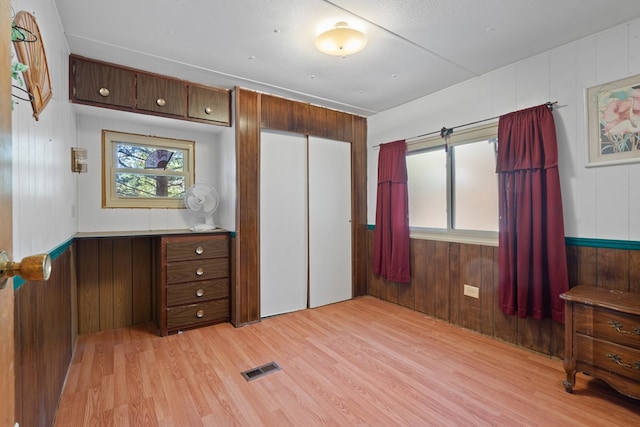 bedroom with a closet, light hardwood / wood-style floors, and wood walls