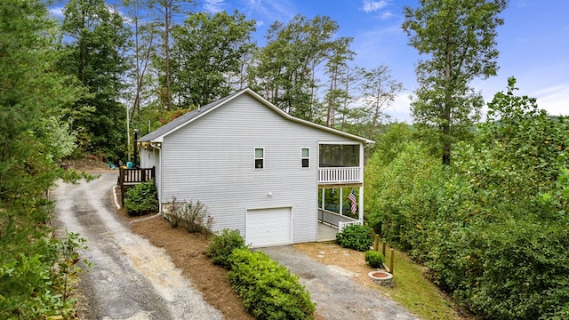 view of side of home with asphalt driveway, an attached garage, and view of wooded area