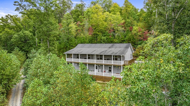 rear view of property featuring a balcony, a forest view, and a sunroom