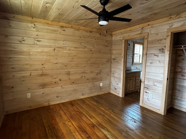 unfurnished bedroom with connected bathroom, wood walls, wooden ceiling, dark hardwood / wood-style flooring, and ceiling fan