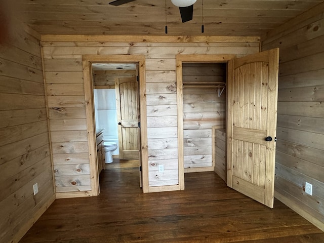 unfurnished bedroom featuring dark wood-type flooring, ensuite bath, and wooden walls