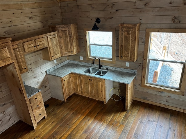 kitchen with sink, wooden walls, light stone countertops, and dark hardwood / wood-style floors