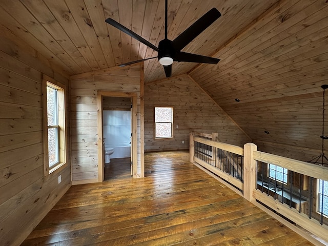 additional living space with lofted ceiling, wood ceiling, wooden walls, dark hardwood / wood-style flooring, and ceiling fan