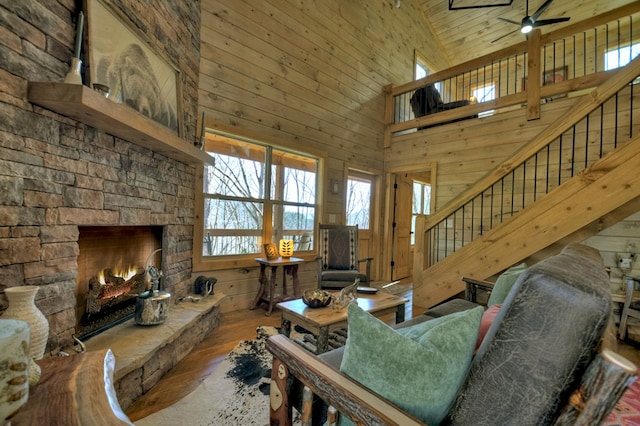 living room featuring ceiling fan, a stone fireplace, wooden walls, and high vaulted ceiling