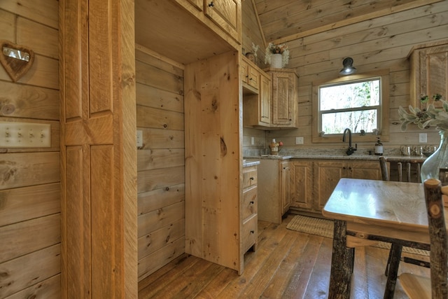 kitchen featuring sink, light hardwood / wood-style flooring, light stone counters, and wood walls