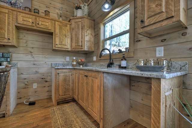 kitchen with light hardwood / wood-style flooring, sink, light stone counters, and wooden walls