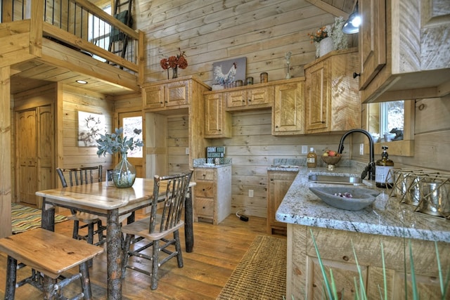 kitchen featuring sink, light hardwood / wood-style flooring, wooden walls, a high ceiling, and light stone countertops