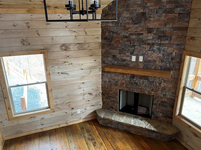 unfurnished living room with hardwood / wood-style flooring, wooden walls, and a stone fireplace