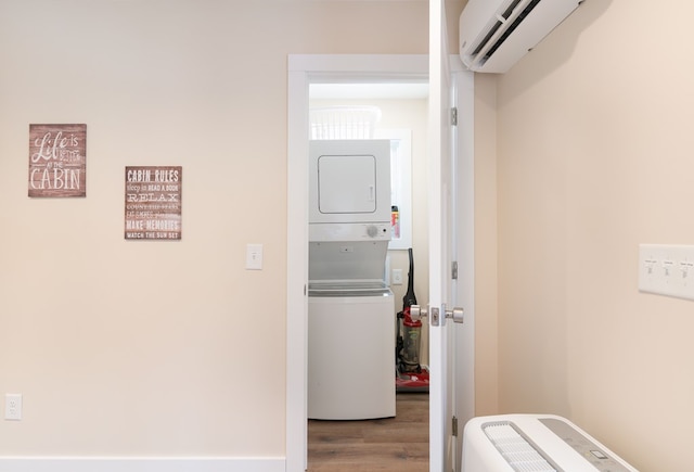 clothes washing area featuring laundry area, a wall mounted AC, stacked washing maching and dryer, and wood finished floors