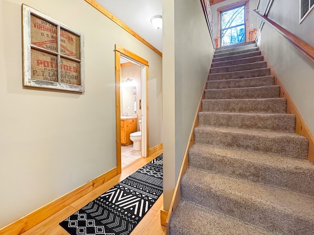 stairs featuring wood finished floors, baseboards, and ornamental molding