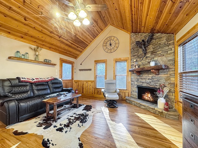 living room featuring a wainscoted wall, wood-type flooring, a stone fireplace, and wooden ceiling