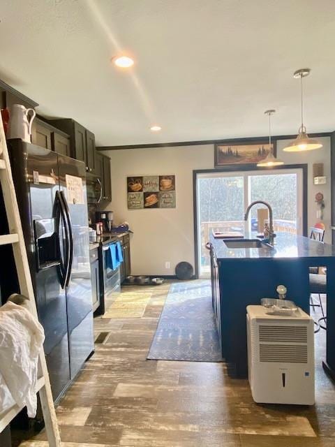 kitchen featuring sink, light wood-type flooring, an island with sink, appliances with stainless steel finishes, and decorative light fixtures