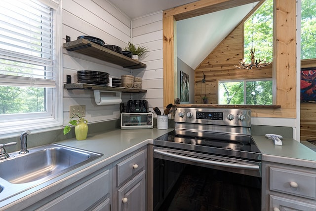 kitchen with stainless steel electric range, lofted ceiling, wooden walls, sink, and gray cabinetry