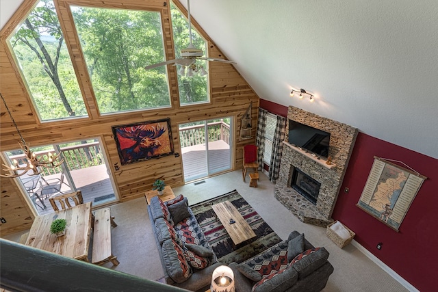 carpeted living room with wood walls, a stone fireplace, high vaulted ceiling, and a notable chandelier