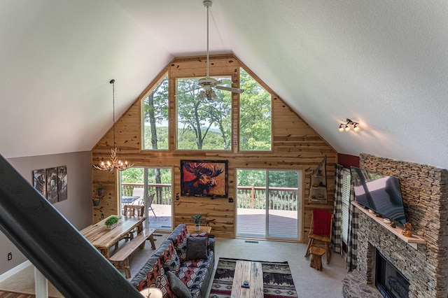 carpeted living room with ceiling fan with notable chandelier, a textured ceiling, high vaulted ceiling, a fireplace, and wooden walls