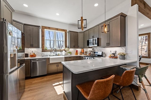 kitchen with appliances with stainless steel finishes, light wood-style floors, a peninsula, and a sink