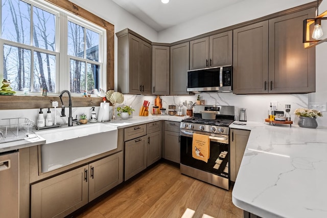 kitchen with light stone counters, a sink, decorative backsplash, light wood-style floors, and appliances with stainless steel finishes