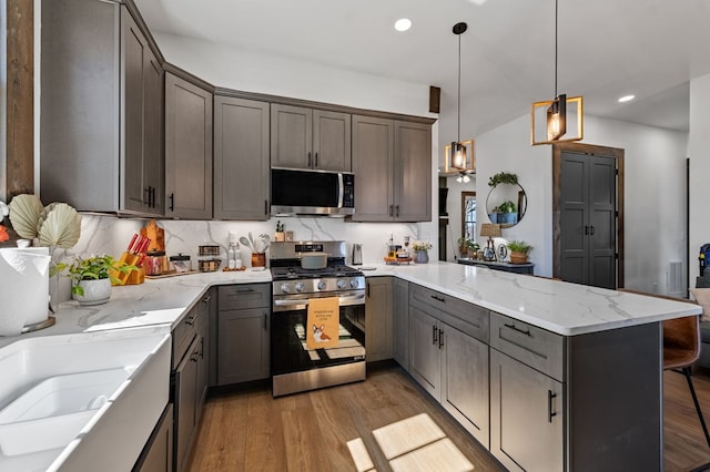 kitchen featuring light wood finished floors, a peninsula, stainless steel appliances, and light stone countertops