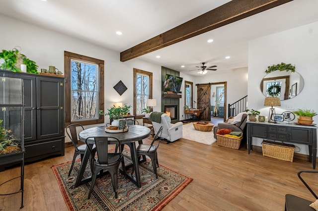 dining area featuring a glass covered fireplace, beamed ceiling, light wood-style floors, and a wealth of natural light