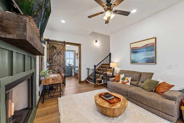 living room with stairway, a barn door, recessed lighting, light wood-style floors, and a ceiling fan