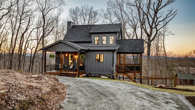 view of front of home with roof with shingles, a sunroom, a chimney, dirt driveway, and board and batten siding