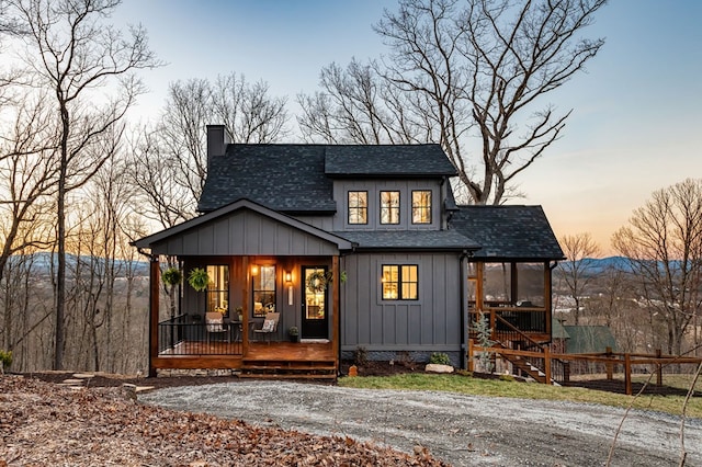 back of house with board and batten siding, fence, roof with shingles, covered porch, and a chimney