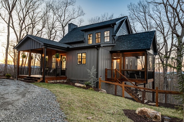 back of house with board and batten siding, a porch, roof with shingles, a chimney, and a yard