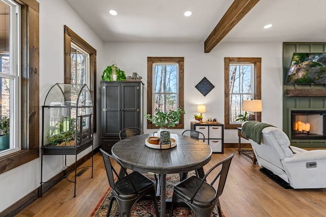 dining space with beamed ceiling, baseboards, a large fireplace, and light wood-style floors