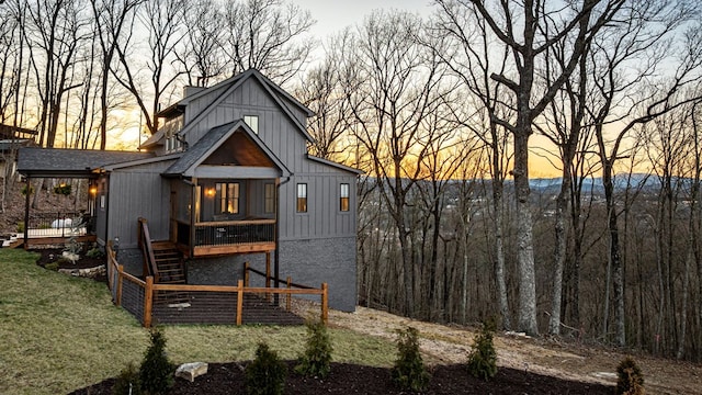 back of property at dusk featuring roof with shingles, a yard, stairs, a deck, and board and batten siding