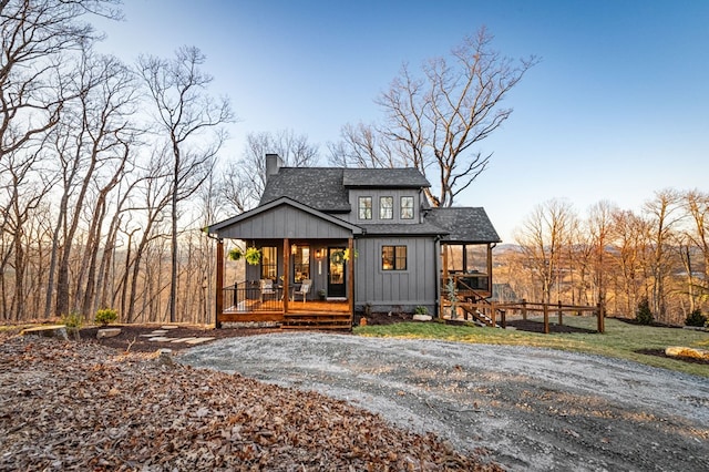 view of front of property featuring board and batten siding, a porch, roof with shingles, a chimney, and driveway