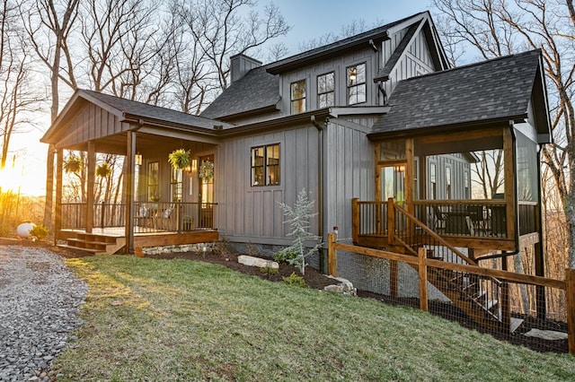 back of house featuring a porch, a yard, roof with shingles, board and batten siding, and a chimney