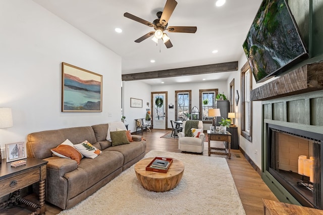 living area featuring a ceiling fan, light wood finished floors, beam ceiling, recessed lighting, and a fireplace