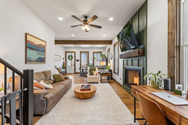 living area with ceiling fan, beamed ceiling, recessed lighting, a fireplace, and light wood-style floors