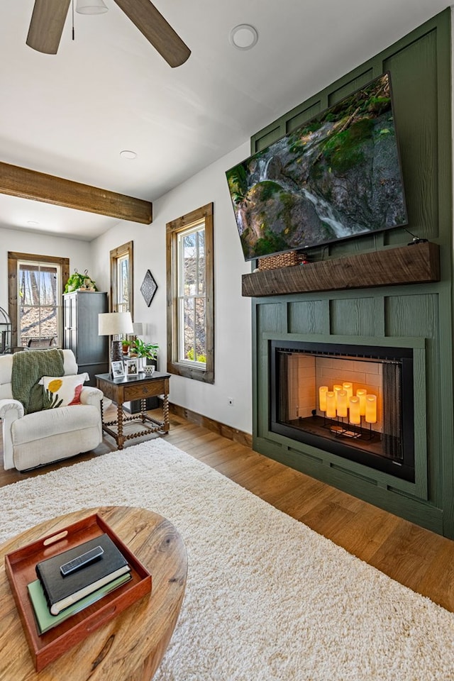 living room with beam ceiling, a ceiling fan, wood finished floors, a fireplace, and baseboards