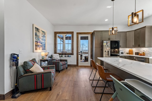 kitchen with light stone counters, a kitchen breakfast bar, stainless steel appliances, light wood-style floors, and hanging light fixtures