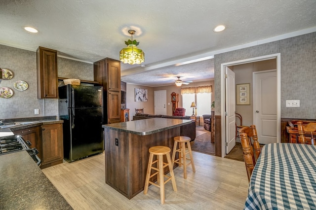 kitchen featuring black refrigerator, a kitchen breakfast bar, gas range oven, and a textured ceiling