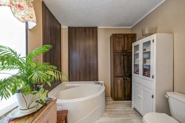 bathroom with hardwood / wood-style floors, a bathing tub, ornamental molding, a textured ceiling, and toilet