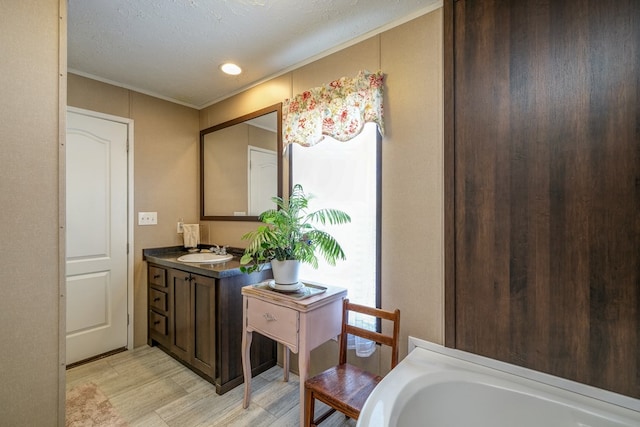 bathroom with a textured ceiling, ornamental molding, vanity, a bath, and hardwood / wood-style floors