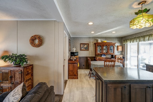 kitchen with light wood-type flooring, ornamental molding, a center island, dark brown cabinetry, and a textured ceiling