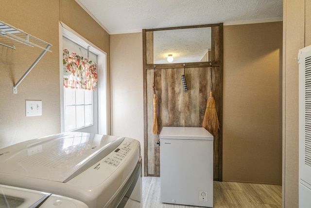 laundry room with ornamental molding, a textured ceiling, independent washer and dryer, and light hardwood / wood-style flooring