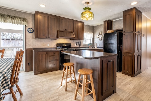 kitchen featuring a breakfast bar, dark brown cabinetry, black appliances, a kitchen island, and custom exhaust hood