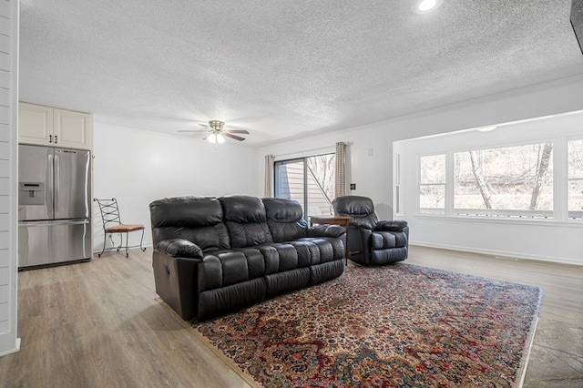 living area featuring ceiling fan, baseboards, light wood finished floors, and a textured ceiling