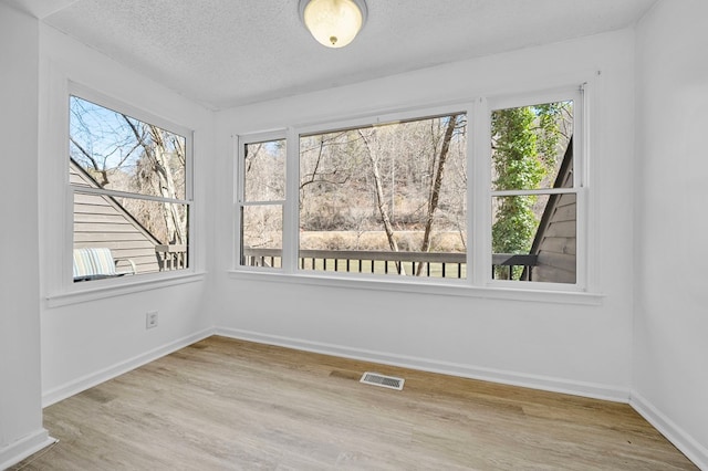 spare room featuring baseboards, wood finished floors, visible vents, and a textured ceiling