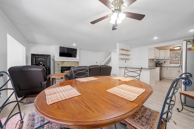 dining area with crown molding, stairway, a lit fireplace, recessed lighting, and light wood-style floors